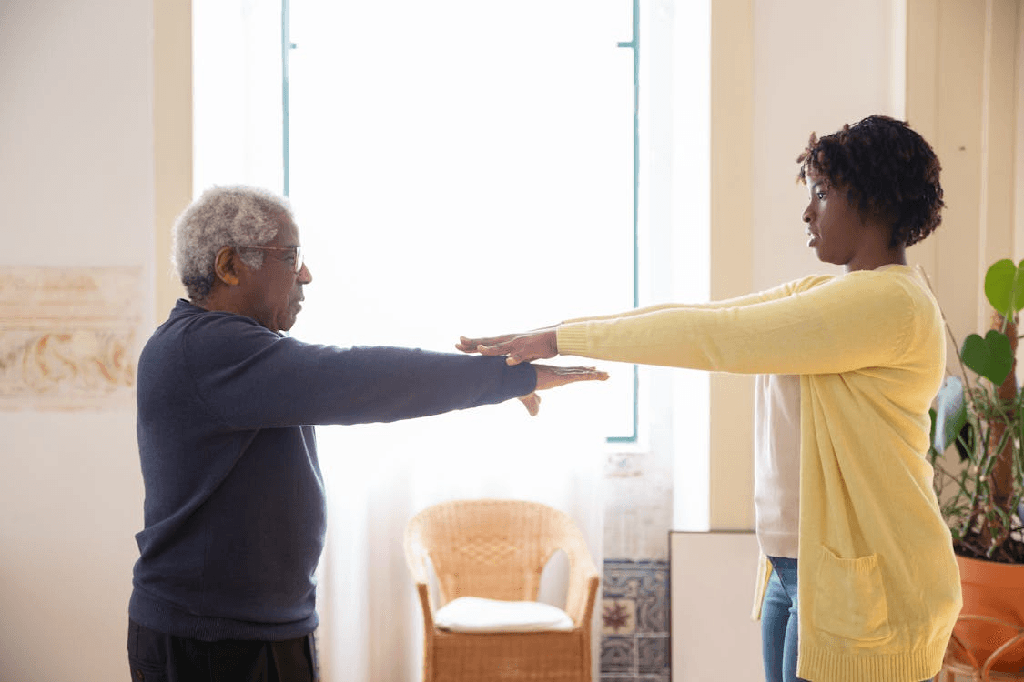 an old man with a caretaker in a yellow sweater doing physical therapy