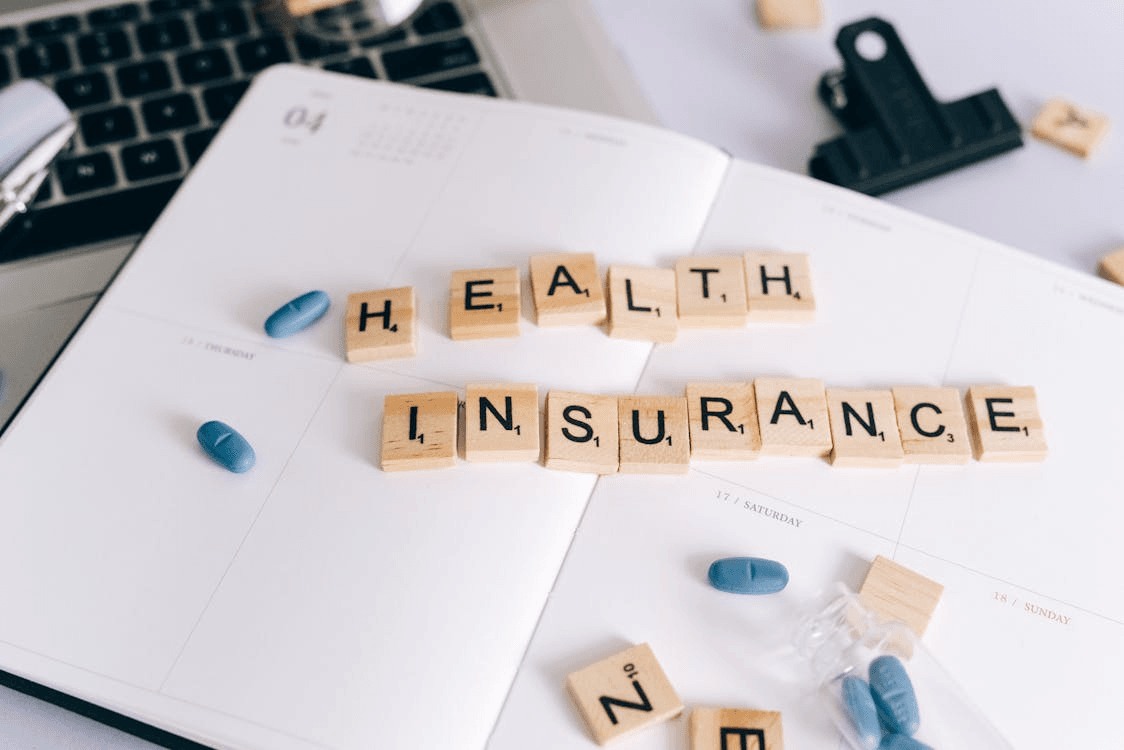  a notebook with pills and Scrabble tiles on it spelling health insurance