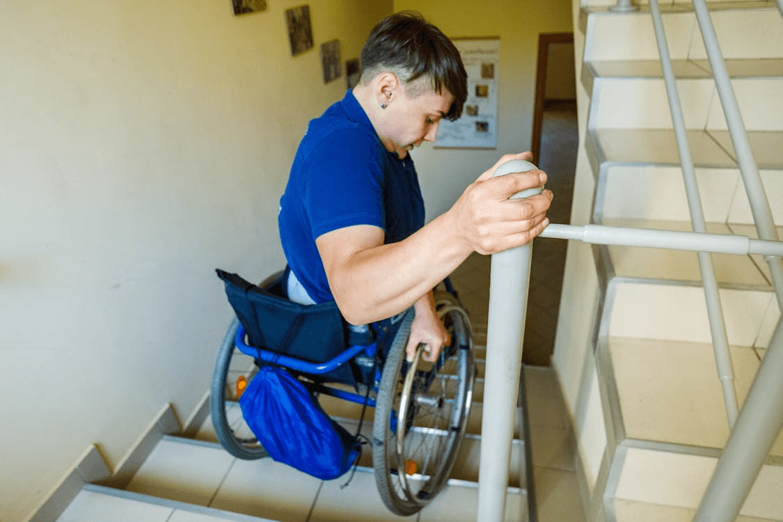 : a man in a blue shirt in a wheelchair trying to get down the staircase on his own