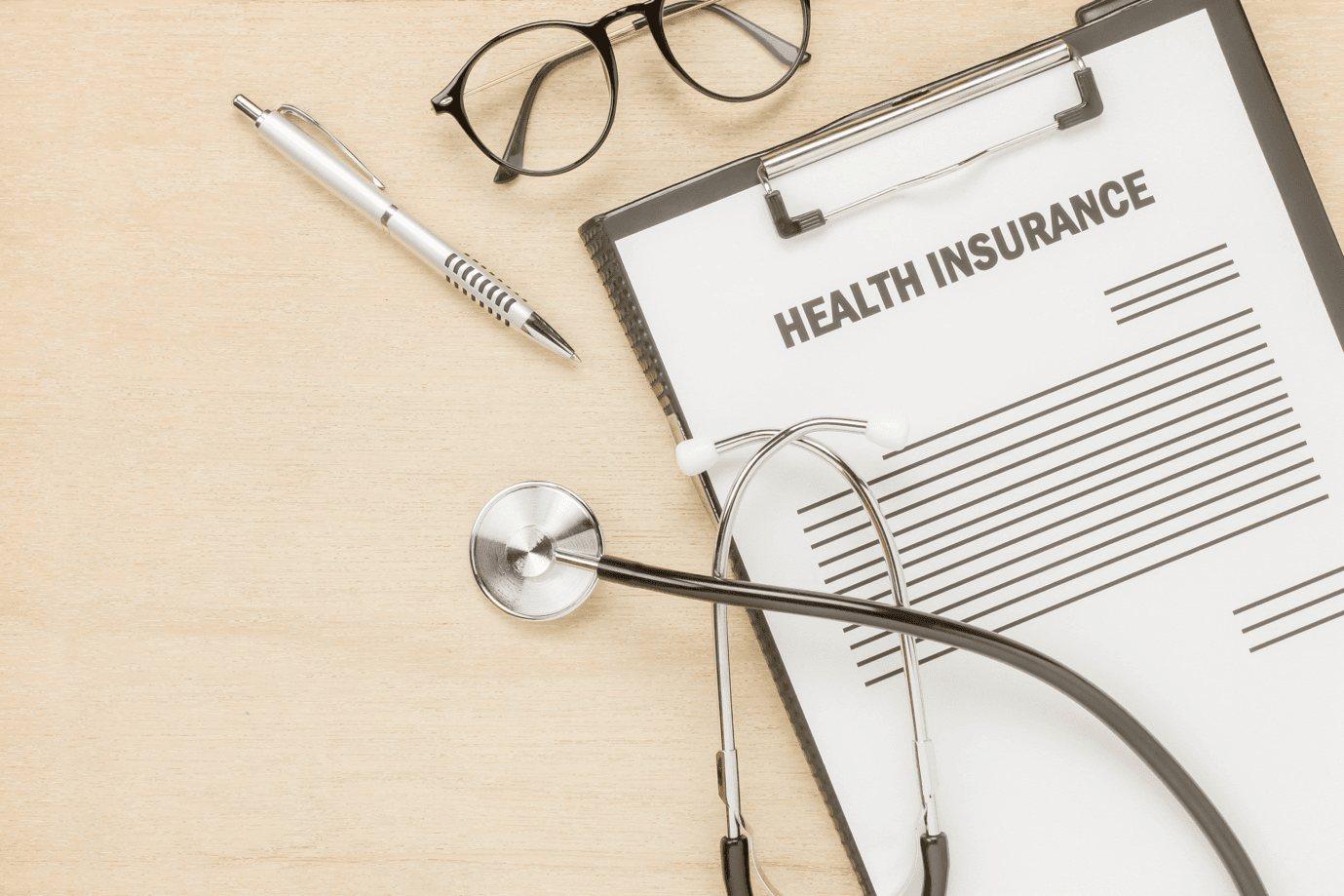 Health insurance forms on a board with a stethoscope, glasses, and a pen