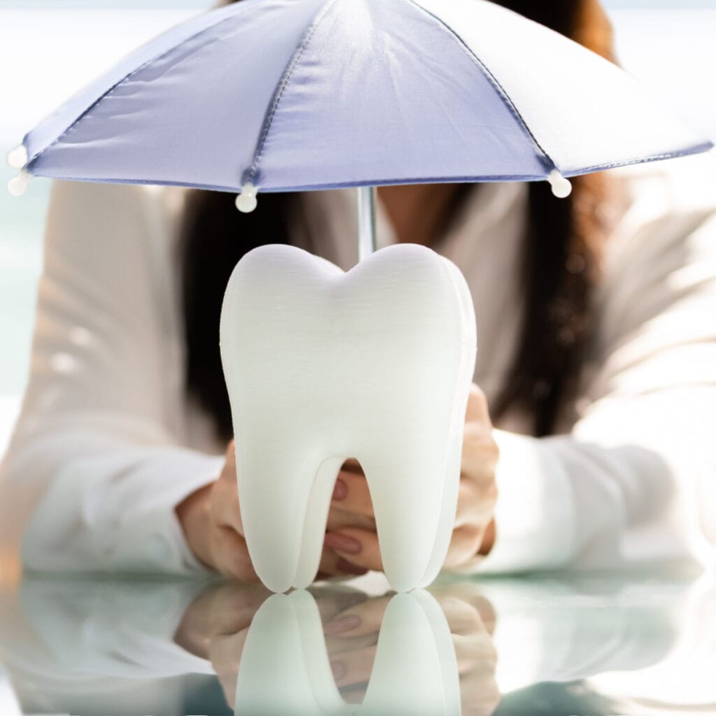 Tooth model with umbrella representing Dental Insurance Plans in Texas coverage options.